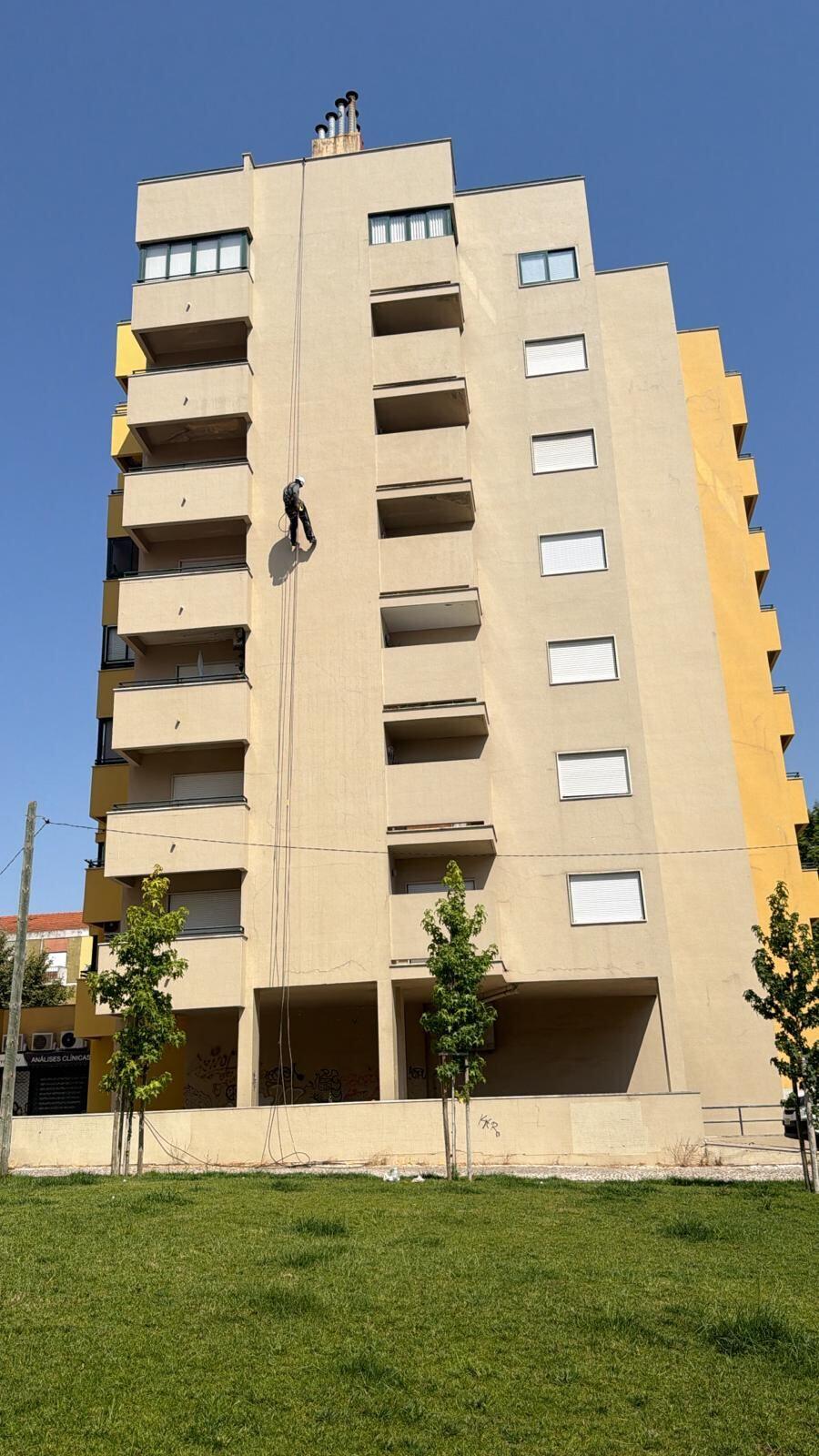 Alpinista industrial a pintar a fachada de um prédio em Lisboa