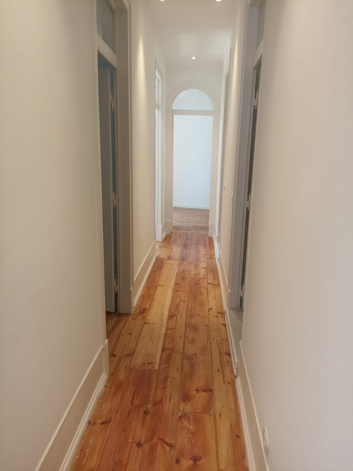Corredor de apartamento com paredes pintadas de branco e soalho recuperado, obra da RJ Vertical